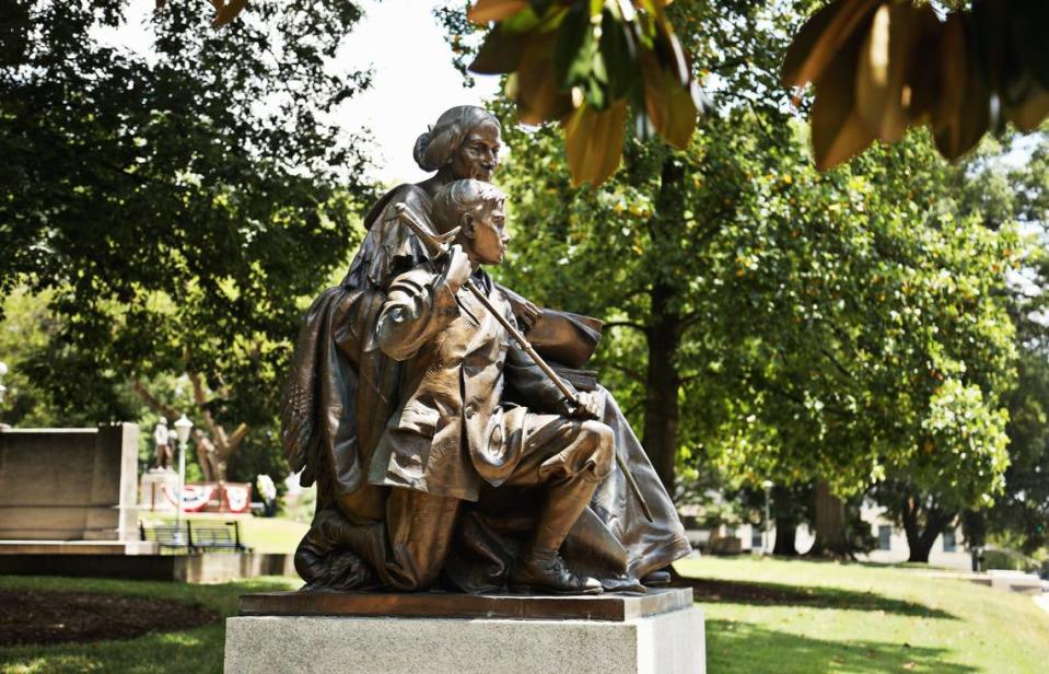 The Confederate Women’s Monument was dedicated June 10, 1914. The monument is a statue of a seated woman and a child — a boy holding a sword. It faces the street, and has two stone benches facing each other, flanking the monument.