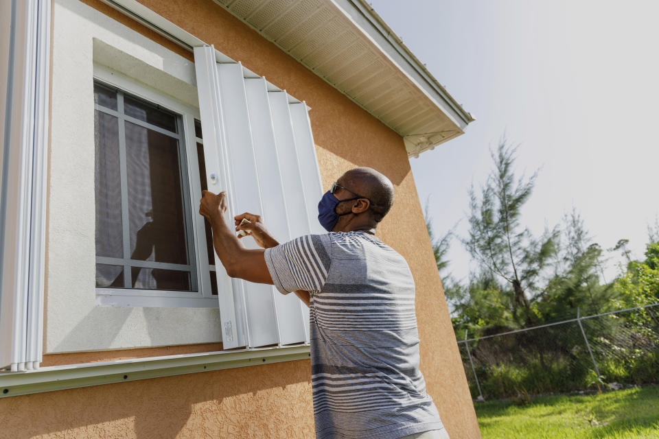 Wendell Smith unfolds his storm shutters over a window on his Arden Forest home in preparation for the arrival of Hurricane Isaias, in Freeport, Grand Bahama, Bahamas, Friday, July 31, 2020. (AP Photo/Tim Aylen)