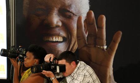 Photographers take pictures in front of a poster of anti-apartheid leader and former president Nelson Mandela during a news conference with the cast of the biographical film "Mandela: Long Walk to Freedom" at the Nelson Mandela Centre of Memory in Johannesburg, November 2, 2013. REUTERS/Siphiwe Sibeko