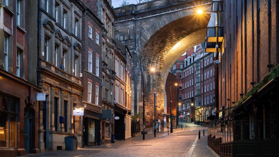 An empty street lined with tall buildings leading up to a viaduct 