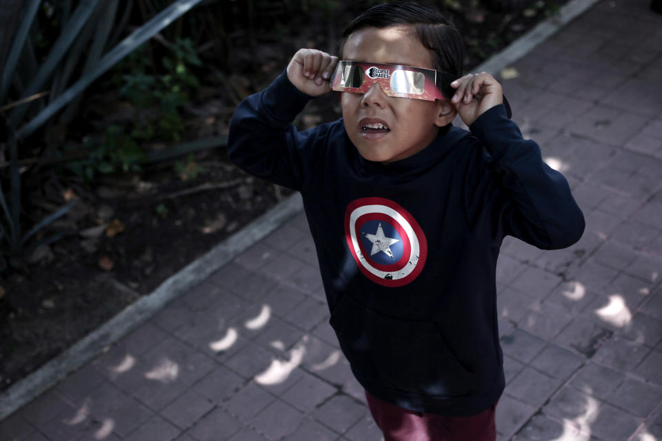 a small child holds cardboard glasses to their face while looking upward