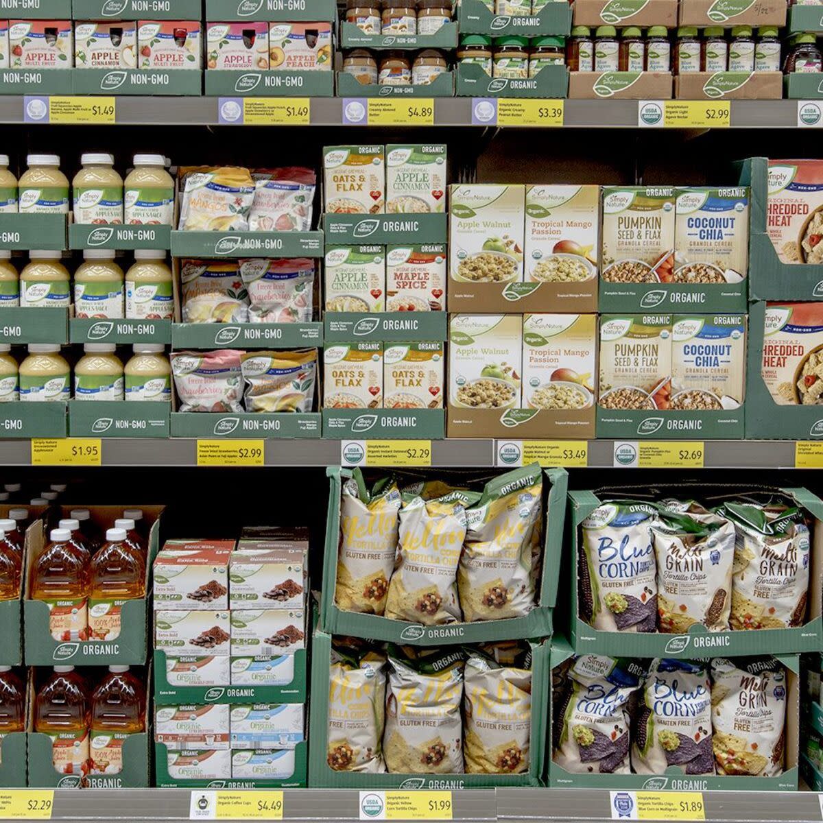 Three aisles of Aldi’s simply nature organic food items in an Aldi including chips, apple juice, oatmeal, and cereal, clean and well organized in dark green cardboard