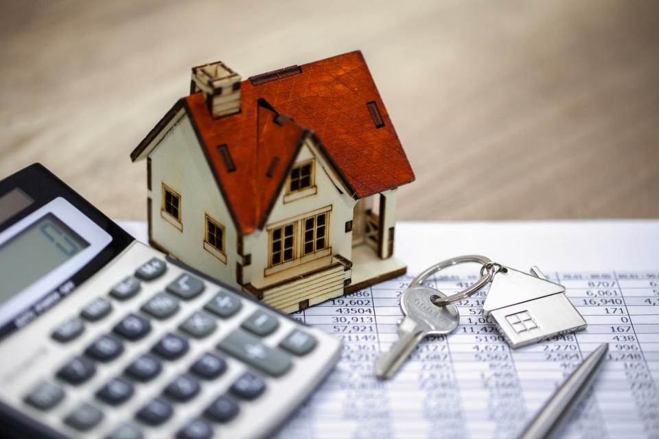 A calculator, house key and a model house sitting on a desk.