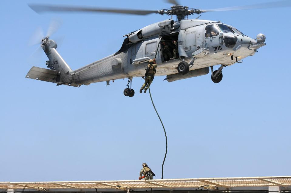 A Navy SEAL descends a rope hanging from a flying helicopter.