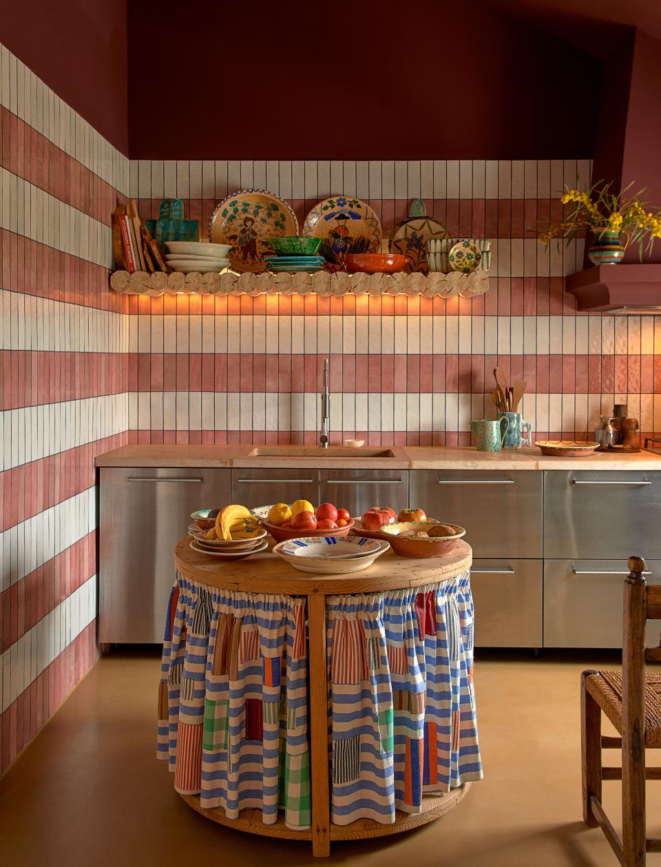 Open shelving is best used not for tight, maximized storage solutions, but for cookware, dishes, and other kitchen decor and accoutrement that is pleasing to the eye. You can use these decor pieces to establish or tie into your kitchen’s color palette, as is the case in <a href="https://www.architecturaldigest.com/story/demeyer-portugal-escape?mbid=synd_yahoo_rss" rel="nofollow noopener" target="_blank" data-ylk="slk:Belgian designer Jean-Philippe Demeyer’s kitchen;elm:context_link;itc:0" class="link ">Belgian designer Jean-Philippe Demeyer’s kitchen</a>, which contrasts its pink-and-white tiled walls with blue accents on its floating shelf and the curtains around its circular island.