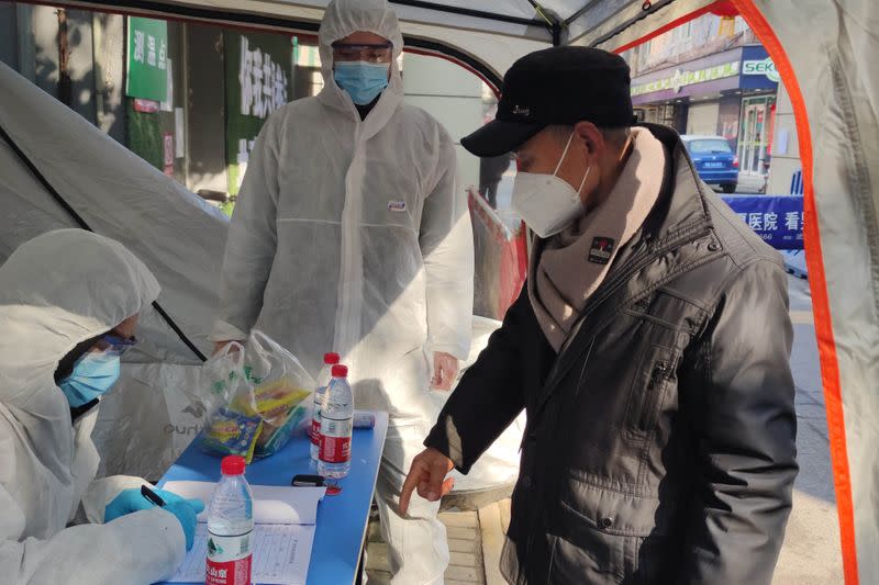 Volunteers in protective suits help a man with registration at a checkpoint of a residential compound, following the outbreak of the novel coronavirus in Wuhan