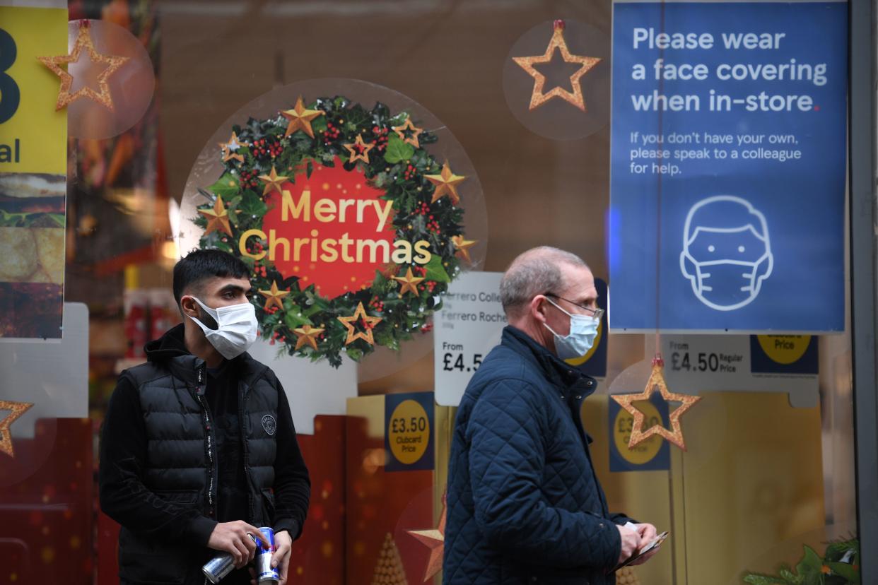 Pedestrians wearing masks because of the novel coronavirus pandemic walk past the window of a closed shop displaying Christmas decoration in the centre of Manchester, northwest England, on November 26, 2020. - London will escape the tightest restrictions once England's national coronavirus lockdown ends next week, the government said Thursday, but major cities including Manchester and Birmingham face at least two more weeks of tough rules. England will return to a regional tiered system when the national regulations end on December 2, with those areas suffering the worst case rates entering the highest Tier 3. (Photo by Oli SCARFF / AFP) (Photo by OLI SCARFF/AFP via Getty Images)