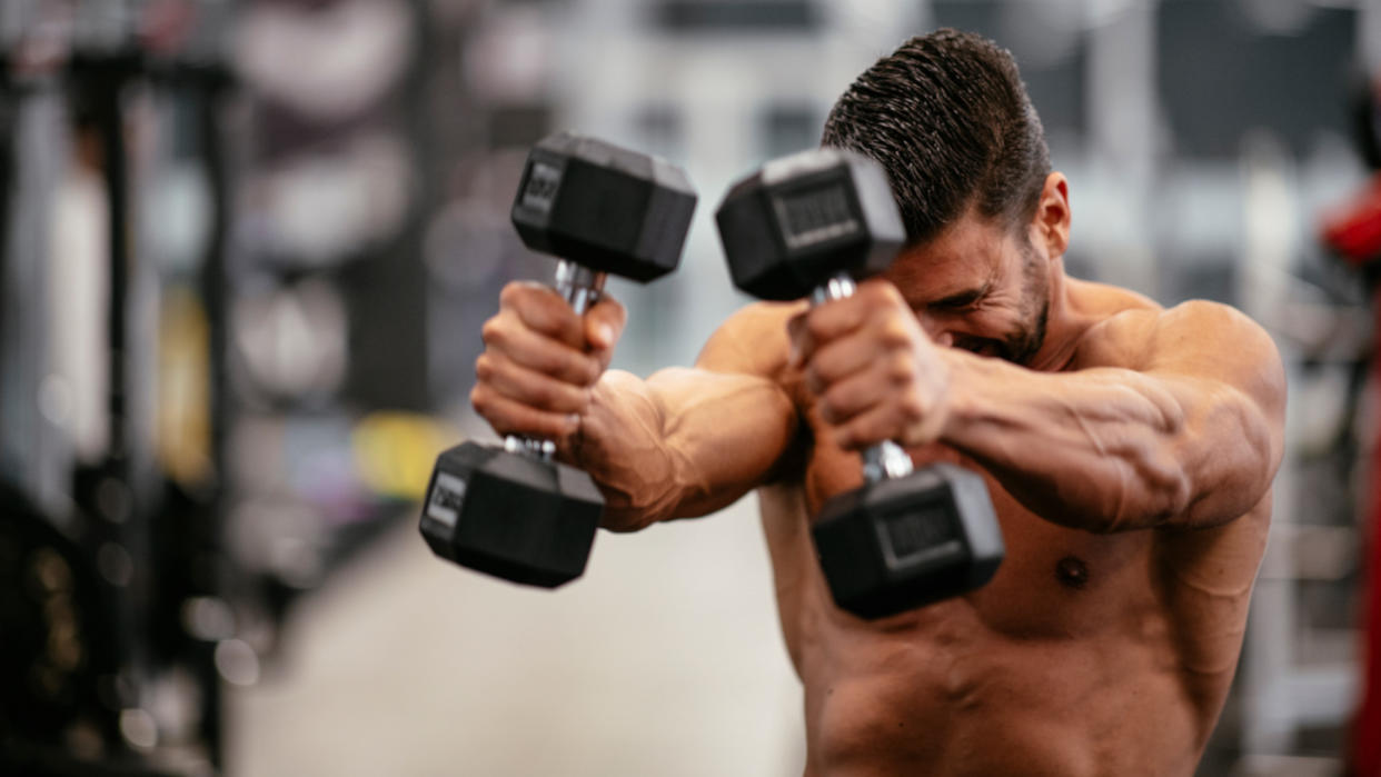  Man performing dumbbell front raises in a gym. 