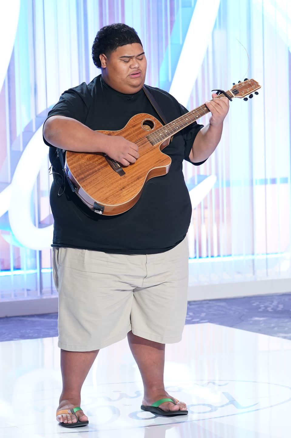 iam tongi playing a guitar while singing in front of an american idol backdrop
