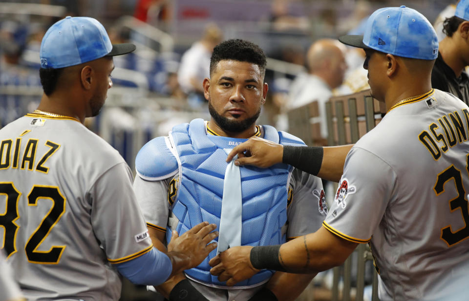 Pittsburgh Pirates' Melky Cabrera, center, tries on Elias Diaz' (32) chest protector as Diaz and Jose Osuna, right, straighten an attached tie on it during the seventh inning of a baseball game against the Miami Marlins, Sunday, June 16, 2019, in Miami. (AP Photo/Wilfredo Lee)