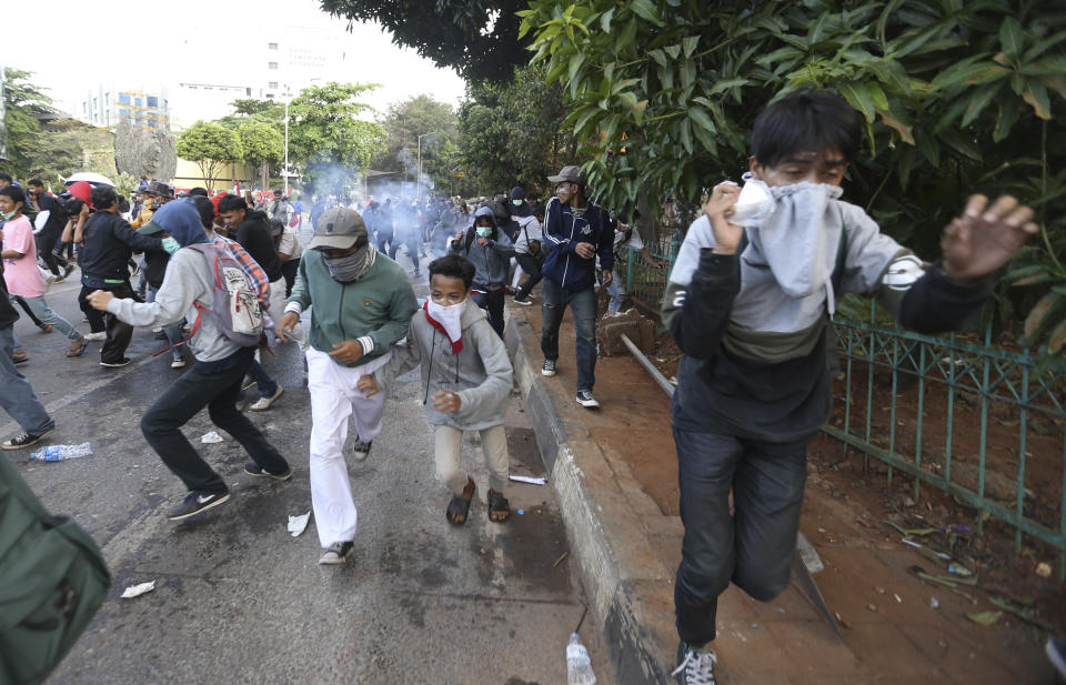 Student protesters run from tear gas fired by riot police during a clash in Jakarta, Indonesia, Monday, Sept. 30, 2019. Thousands of Indonesian students resumed protests on Monday against a new law they say has crippled the country's anti-corruption agency, with some clashing with police.(AP Photo/Achmad Ibrahim)