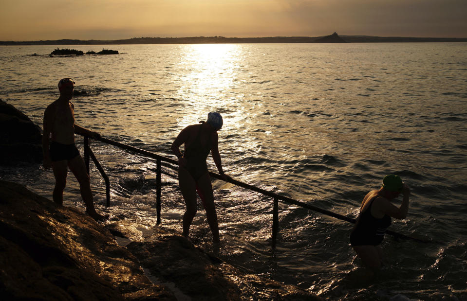 People prepare to enter the sea in Penzance, Cornwall, England, Monday July 18, 2022. The British government have issued their first-ever "red" warning for extreme heat. The alert covers large parts of England on Monday and Tuesday, when temperatures may reach 40 degrees Celsius (104 Fahrenheit) for the first time, posing a risk of serious illness and even death among healthy people, the U.K. Met Office, the country's weather service, said Friday. (Ben Birchall/PA via AP)