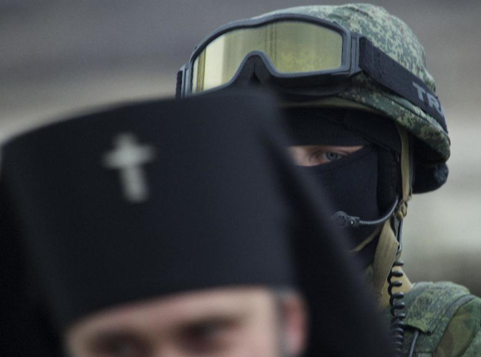 Russian solder is seen behind Ukrainian Orthodox Archbishop Clement, foreground, outside of a Ukrainian military base in the village of Perevalne, outside of Simferopol, Ukraine, on Sunday, March 2, 2014. Hundreds of armed men in trucks and armored vehicles surrounded the Ukrainian military base Sunday in Crimea, blocking its soldiers from leaving. (AP Photo/Ivan Sekretarev)