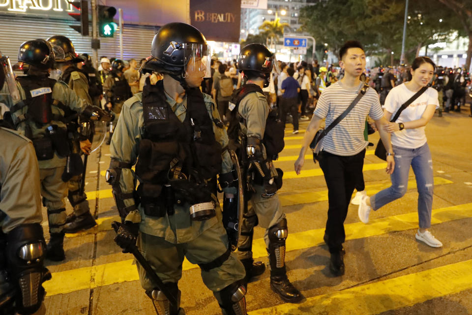 Residents past by police in riot gear during street protests in Hong Kong on Saturday, Aug. 10, 2019. Hong Kong is in its ninth week of demonstrations that began in response to a proposed extradition law but have expanded to include other grievances and demands for more democratic freedoms. (AP Photo/Vincent Thian)