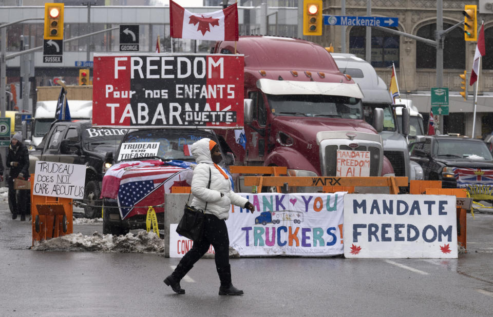 A woman crosses the street in front of vehicles parked as part of the trucker protest, Tuesday, Feb. 8, 2022 in Ottawa. Canadian lawmakers expressed increasing worry about protests over vaccine mandates other other COVID restrictions after the busiest border crossing between the U.S. and Canada became partially blocked. (Adrian Wyld /The Canadian Press via AP)