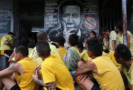 Detainees sit next to a mural of Philippines President Rodrigo Duterte while authorities search through belongings for illegal contraband inside the Manila City Jail in metro Manila, Philippines October 16, 2017. The words on the mural read "Steer away from illegal drugs to save your life and in turn, will save the country's". REUTERS/Romeo Ranoco