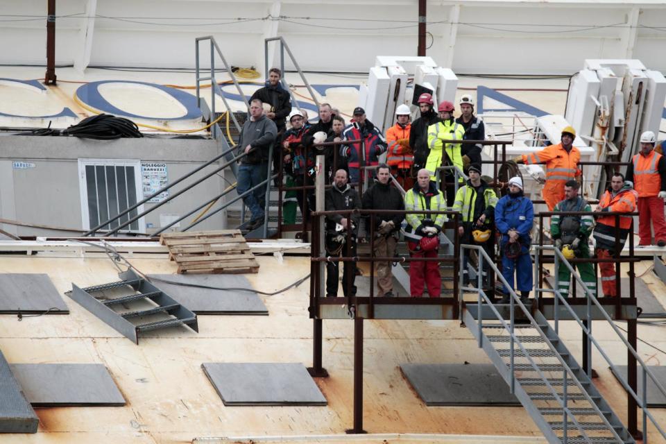 Workers observe a minute silence as they stand on the Costa Concordia cruise ship leaning on its side off the Tuscan Island Isola del Giglio, Italy, Sunday, Jan. 13, 2013. Survivors of the Costa Concordia shipwreck and relatives of the 32 people who died marked the first anniversary of the grounding Sunday. The first event of Sunday's daylong commemoration was the return to the sea of part of the massive rock that tore into the hull of the 112,000-ton ocean liner on Jan. 13, 2012 and remained embedded as the vessel capsized along with its 4,200 passengers and crew. (AP Photo/Gregorio Borgia)