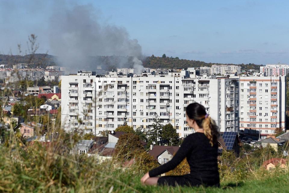 A woman sits on the hill as smoke rises above buildings in the western Ukrainian city of Lviv after a Russian missile strike on October 10, 2022, amid Russian invasion of Ukraine