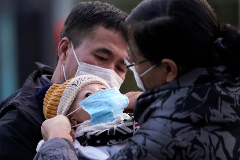 Passengers help a baby wear a mask at the Shanghai railway station