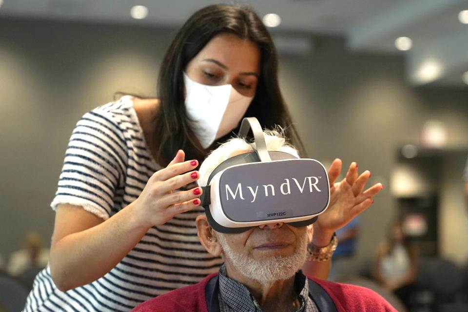 Gloria Gantes, left, adjusts the goggles of resident John Dalsimer as he participates in a virtual reality study at John Knox Village, Tuesday, June 1, 2021, in Pompano Beach, Fla. The senior community is in partnership with Stanford University's Virtual Human Interaction Lab on a study to see how older adults respond to virtual reality and whether it can improve their sense of wellbeing. (AP Photo/Lynne Sladky)