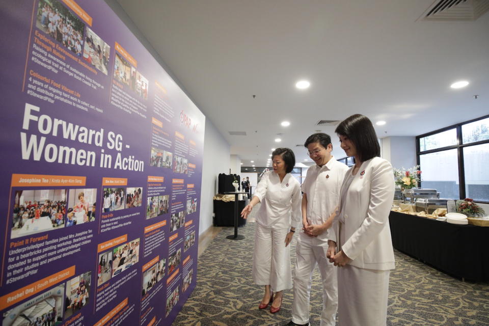 Sim Ann, DPM Lawrence Wong and Sun Xueling at the photo wall which displays the outreach initiatives driven by the women MPs.