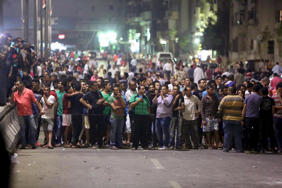 People stand near the site of a bomb blast at a national security building in Shubra Al-Khaima on the outskirts of Cairo, Egypt