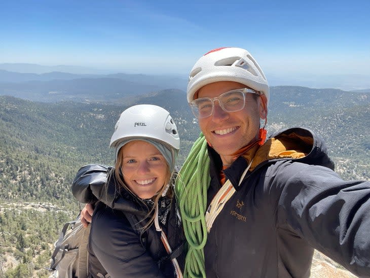 Shmidt and the author smiling, wearing helmets, with a rope draped over them, at the top of Tahquitz Rock.