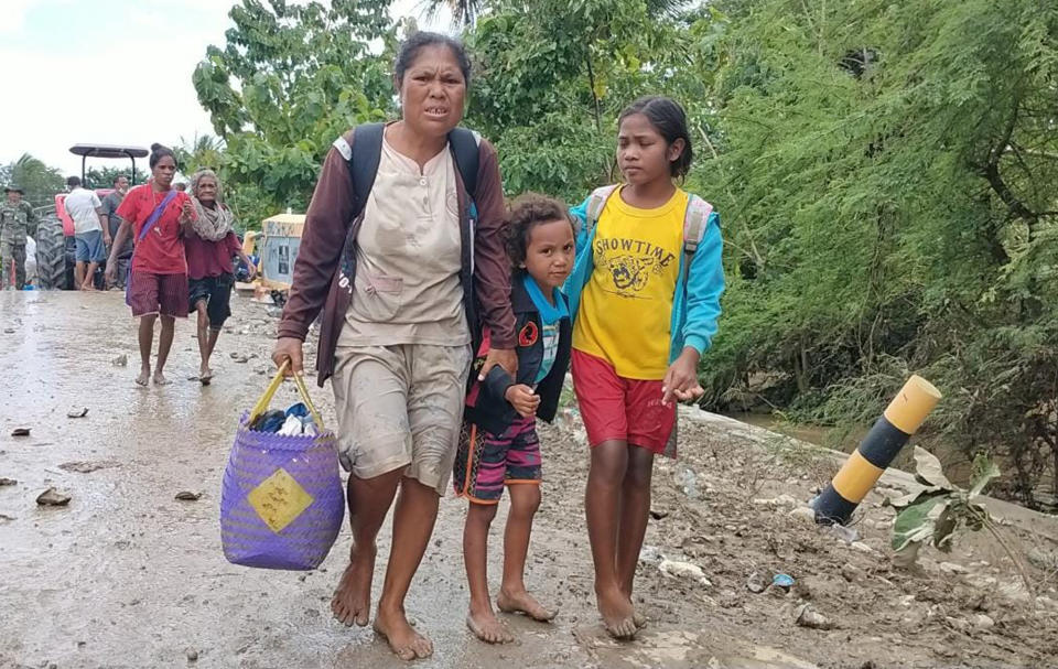 A woman with her children carries their belongings as they walk after crossing a flooded road in Malaka Tengah, East Nusa Tenggara province, Indonesia, Monday, April 5, 2021. Multiple disasters caused by torrential rains in eastern Indonesia have left dozens of people dead and missing and displaced thousands, the country's disaster relief agency said Monday. (AP Photo)