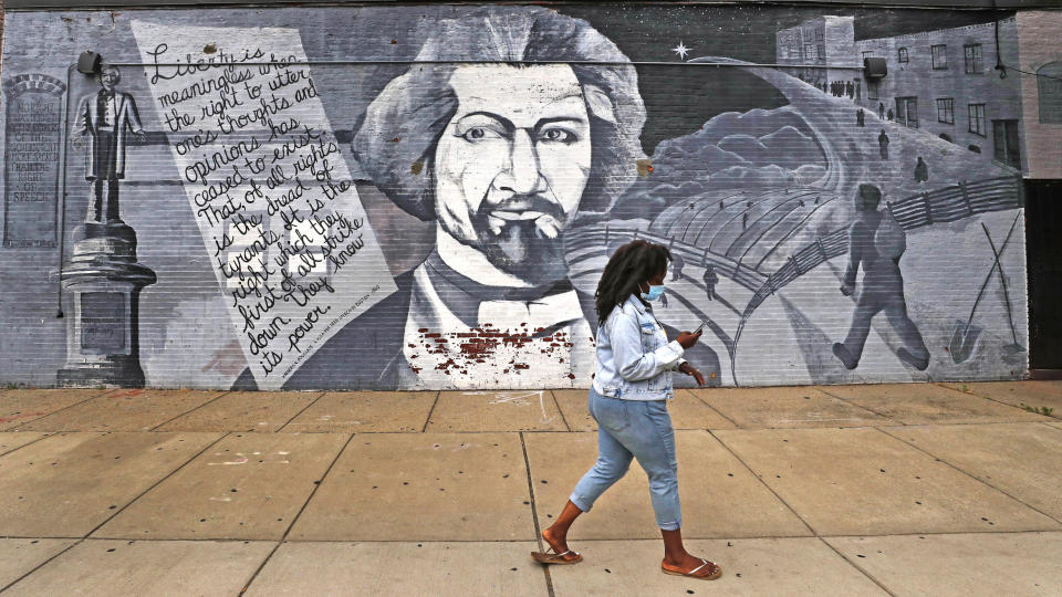 In this Wednesday, June 24, 2020, photograph, a woman walks past a mural in tribute to Frederick Douglass on the exterior wall of the Black-owned Slade's Bar and Grill in the South End neighborhood of Boston. Many from outside Boston have recently ordered takeout, purchased gift cards and supported the restaurant amid nationwide protests against racism. (AP Photo/Charles Krupa)