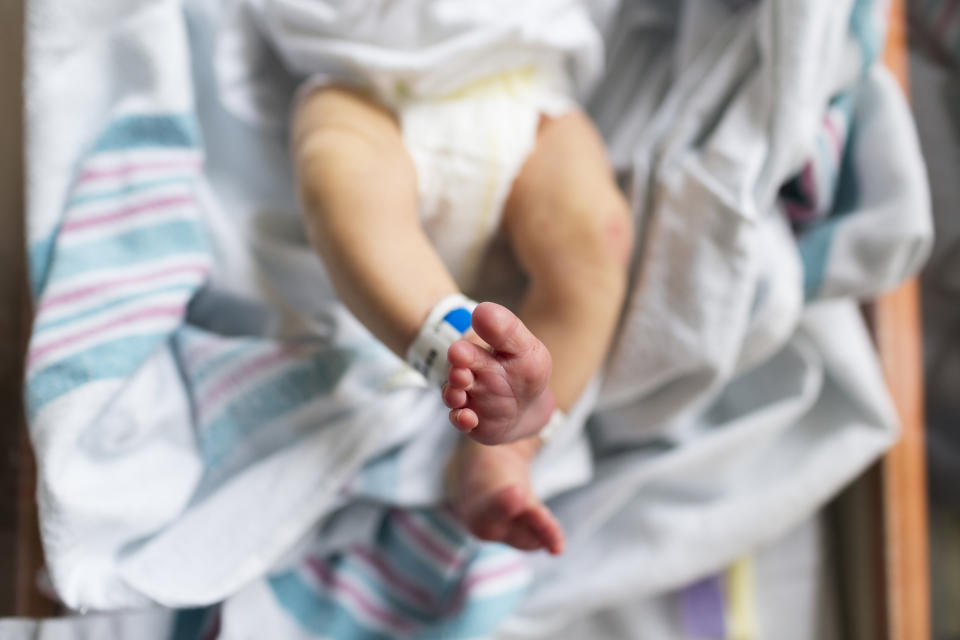 Newborn baby with hospital ID band holding an adult's finger, wrapped in a striped blanket