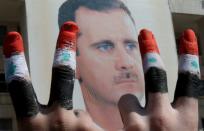 Deux hommes avec les doigts peints dans les couleurs du drapeau syrien font le V de la victoire devant une affiche du président Bachar a-Assad dans le centre de Damas, le 29 mars 2011