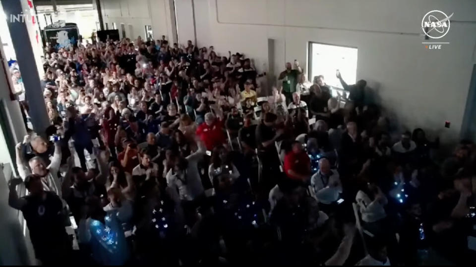 a crowd of people in a packed room celebrate, waving their arms and high-fiving