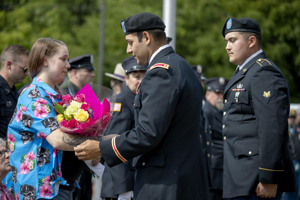 Lt. Patrick Nieto, center, with the Army's 754th Ordnance Company out of Fort Drum, N.Y., presents Krista Johnston with flowers during a memorial service Saturday, Aug. 31, 2019, in Trumansburg, N.Y., for her husband, Sgt. James Johnston, who was killed in Afghanistan in June. Wearing her husband's favorite blue-and-pink Hawaiian shirt; the impossibly young widow returned to her tiny hometown for two milestones: mourning the love of her life, and celebrating the impending birth of their baby. (AP Photo/David Goldman)