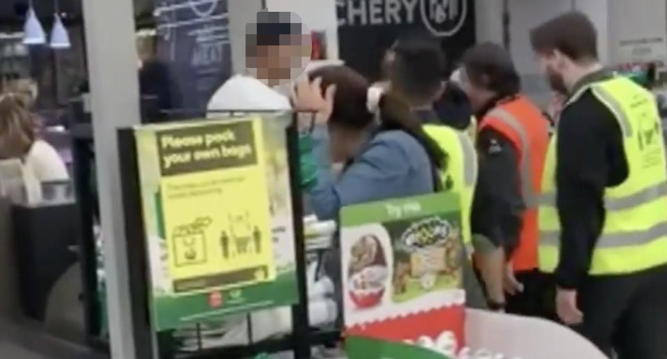 A man, with his face blurred, is escorted out of a Woolworths in Merrylands by staff and security.