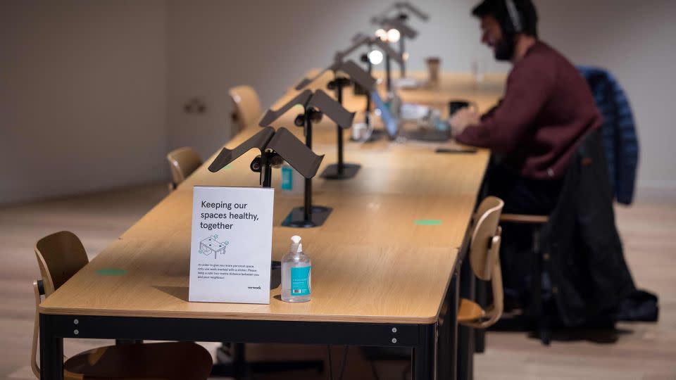 A person works at a shared workspace near signage advising people to maintain social distance at the WeWork, coworking and office space in the City of London, on April 13, 2021, as the company enhances health and safety standards in response to COVID-19. - Tolga Akmen/AFP/Getty Images