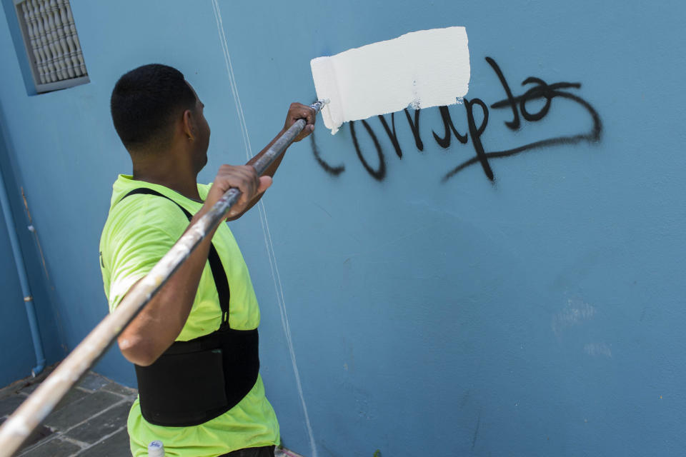 A man paints over the Spanish word "Corrupt" that was painted on a wall, amid protests in San Juan, Puerto Rico, Thursday, July 18, 2019. Protesters are demanding Gov. Ricardo Rossello resign after the leak of online chats that show him making misogynistic slurs and mocking his constituents. (AP Photo/Dennis M. Rivera Pichardo)