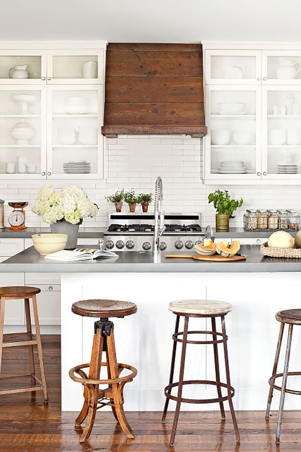 an all white farmhouse kitchen with a warm wood range hood and barstools that are mismatched