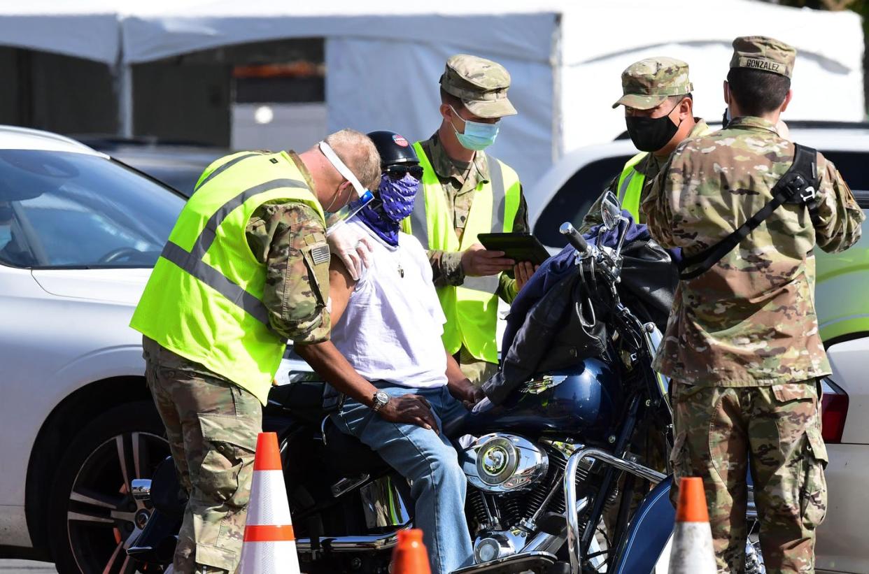 <span class="caption">The National Guard joined forces with FEMA to launch a mass vaccination site in Los Angeles.</span> <span class="attribution"><a class="link " href="https://www.gettyimages.com/detail/news-photo/motorcyclist-receives-his-covid-19-vaccine-administered-by-news-photo/1231206587" rel="nofollow noopener" target="_blank" data-ylk="slk:Frederic J. Brown/AFP via Getty Images;elm:context_link;itc:0;sec:content-canvas">Frederic J. Brown/AFP via Getty Images</a></span>