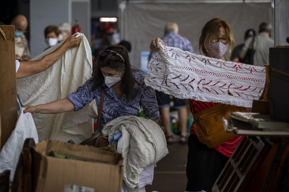Customers wearing face masks pick second hand fabrics in a market in Barcelona on Wednesday, July 8, 2020. Spain's northeastern Catalonia region will make mandatory the use of face masks outdoors even when social distancing can be maintained, regional chief Quim Torra announced Wednesday. (AP Photo/Emilio Morenatti)