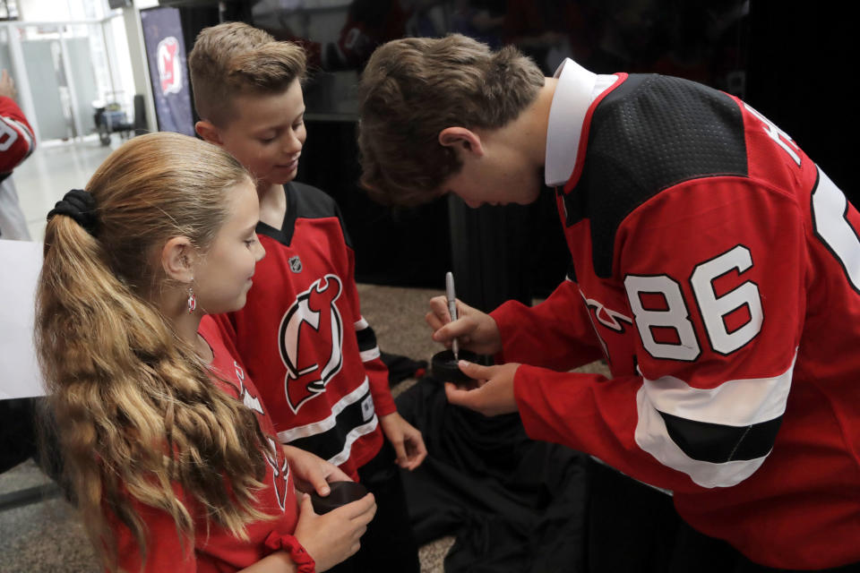 New Jersey Devils forward Jack Hughes, right, the No. 1 overall pick in the 2019 NHL hockey draft, signs autographs for Nicholas Palumbo, 12, center, and his sister Grace Palumbo, 10, from Nutley, N.J., after a news conference introducing the prospect to local media, Tuesday, June 25, 2019, in Newark, N.J. After getting the autograph, Nicholas Palumbo headed out to partake in his sixth grade graduation from Spring Garden Elementary School. (AP Photo/Julio Cortez)