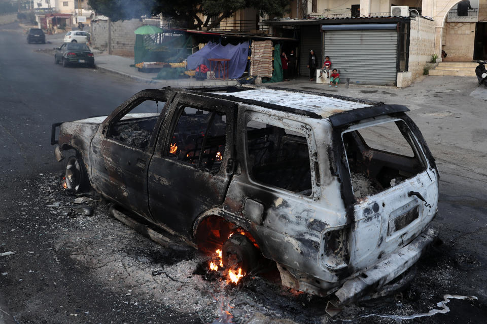 A family looks at a burning car after heavy clashes in the coastal town of Khaldeh, south of Beirut, Lebanon, Sunday, Aug. 1, 2021. At least two people were killed on Sunday south of the Lebanese capital when gunmen opened fire at the funeral of a Hezbollah commander who was killed a day earlier, an official from the group said. (AP Photo/Bilal Hussein)