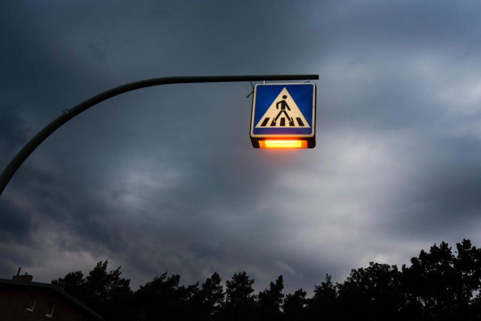 An illuminated traffic sign for a pedestrian crossing can be seen in the evening against a cloudy sky