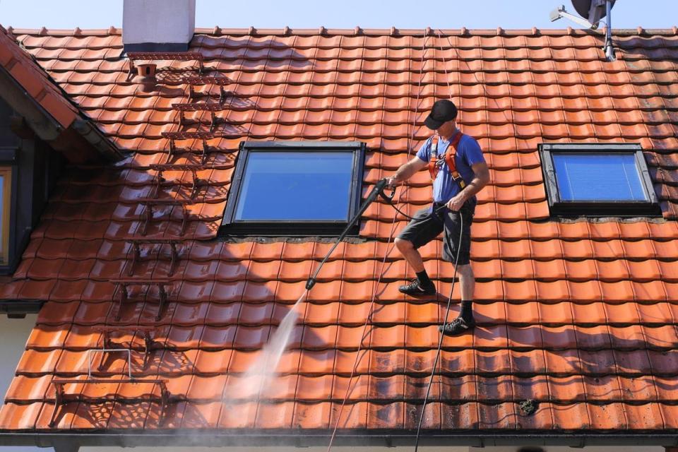 a man power washes a red tiled roof.