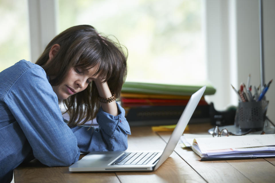 young woman sitting at a desk holding her head in pain