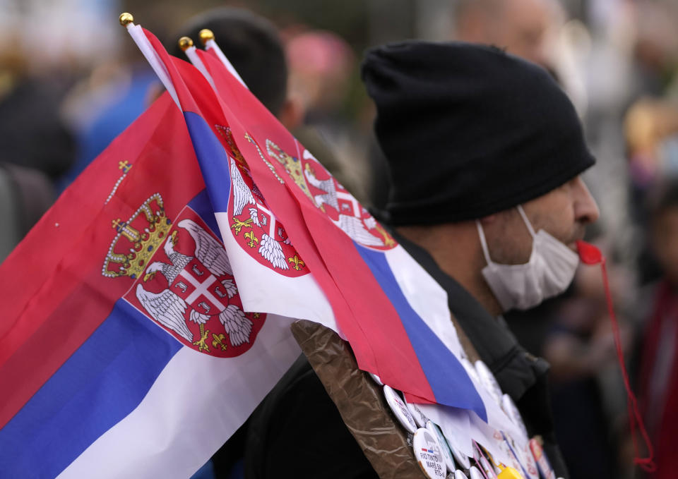A street vendor holds Serbian flags during a protest for clean air in Belgrade, Serbia, Sunday, Nov. 28, 2021. Several thousand people have rallied in Belgrade for another environmental protest, a day after demonstrators blocked bridges and roads on several locations in Serbia, and scuffled with riot police who deployed to stop them. (AP Photo/Darko Vojinovic)