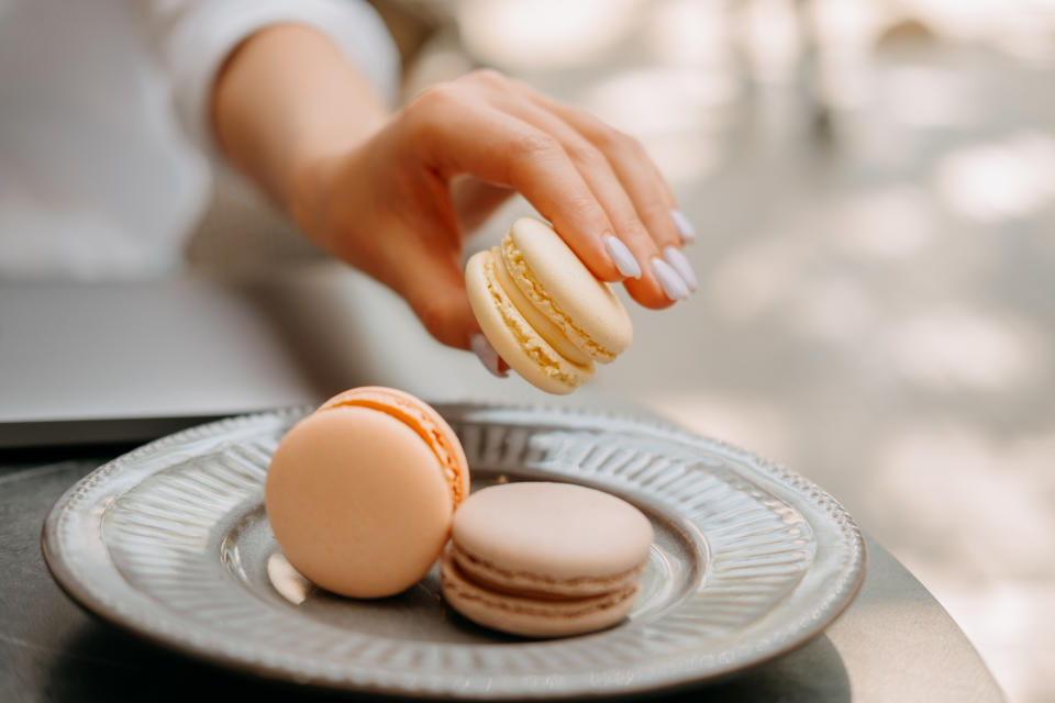 Young female hand is taking gentle a piece of macaron from a cute gray plate.