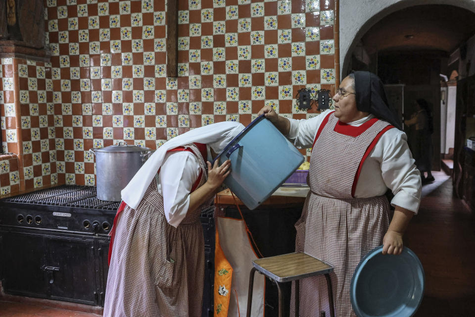 La hermana María de Jesús Frayle, de 24 años, a la izquierda, mete la cabeza en una ollla para oler la comida que sujeta Abigail López, de 29 años, en el convento de las Adoratrices Perpetuas del Santísimo Sacramento en Ciudad de México el viernes 10 de diciembre de 2023. (AP Foto/Ginnette Riquelme)