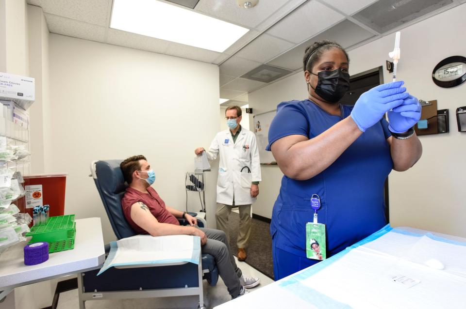 woman in scrubs prepares covid-19 vaccine, with patient and doctor chatting in background