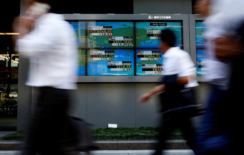 FILE PHOTO: People walk past an electronic board showing Japan's Nikkei average outside a brokerage at a business district in Tokyo