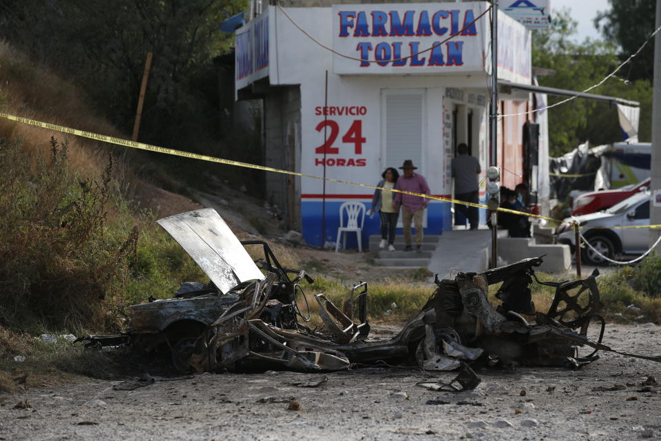 Locals walk past a burned-out car outside the Tula General Hospital, after a gang rammed several vehicles into a prison and escaped with nine inmates, in Tula, Mexico, Wednesday, Dec. 1, 2021. Local media reported that the burned-out cars found in the city after the attack were car bombs. Authorities said they were investigating how the vehicles caught fire. (AP Photo/Ginnette Riquelme)